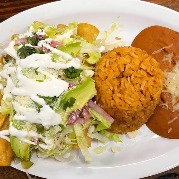 A plate of chilaquiles with rice and beans, topped with lettuce, avocado, sour cream, and cheese.