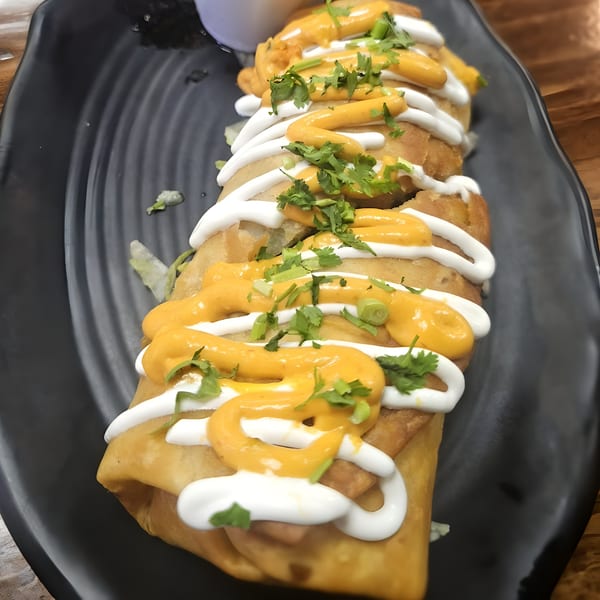 Crispy fried burritos from Taco Shop 760, drizzled with white and orange sauces, garnished with cilantro.