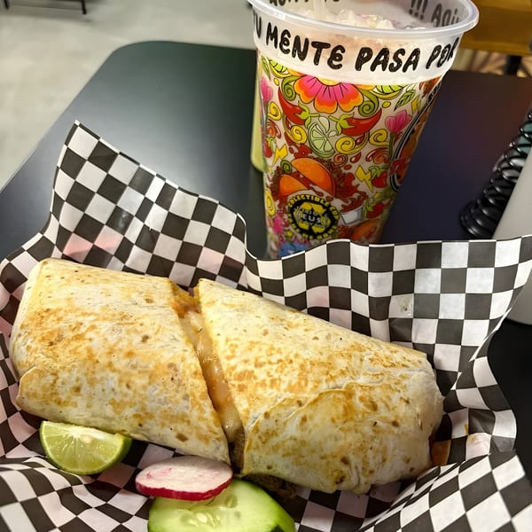 A large quesadilla with lime, radish, and cucumber slices, next to a colorful drink cup.