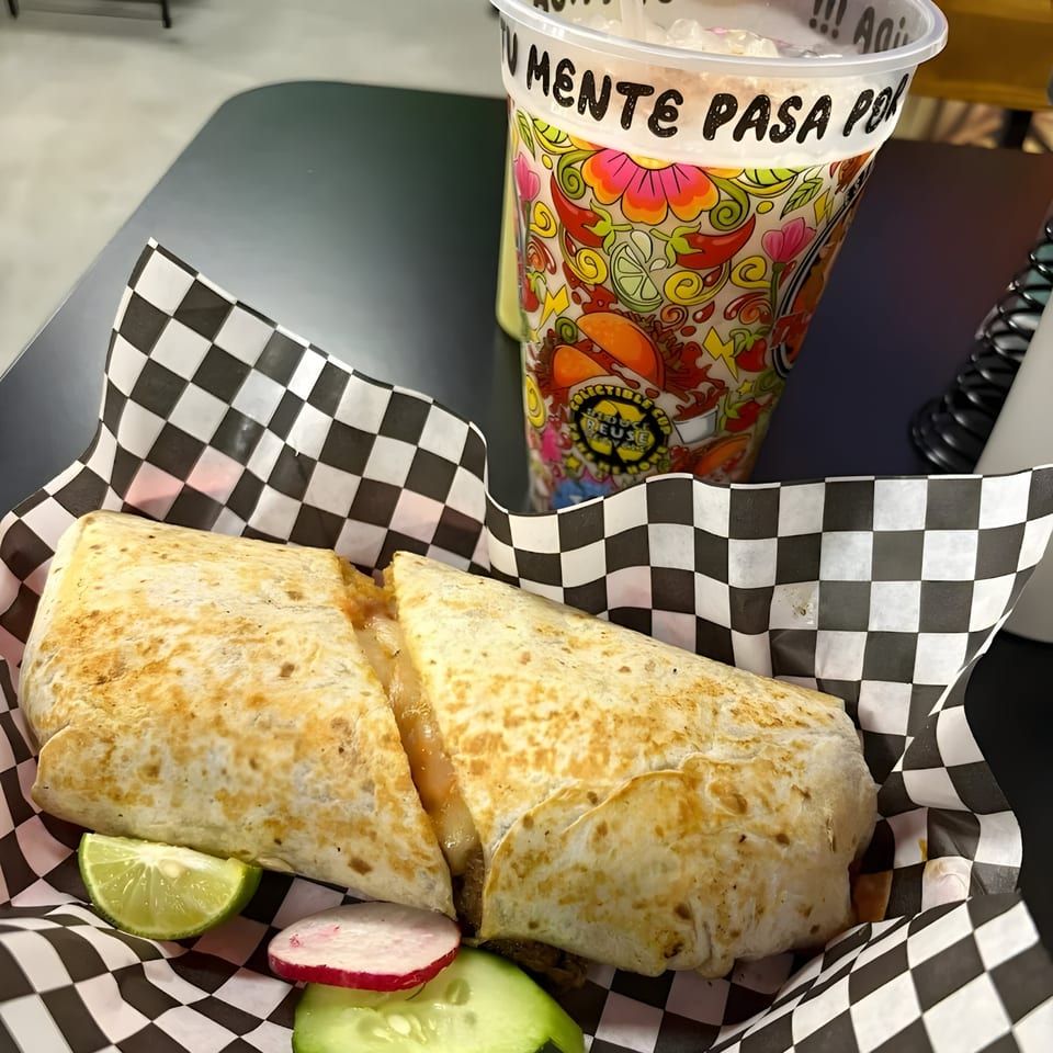 A large quesadilla with lime, radish, and cucumber slices, next to a colorful drink cup.