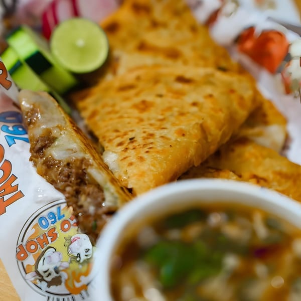Taco Shop 760 birria tacos with lime wedges and a side of consommé.